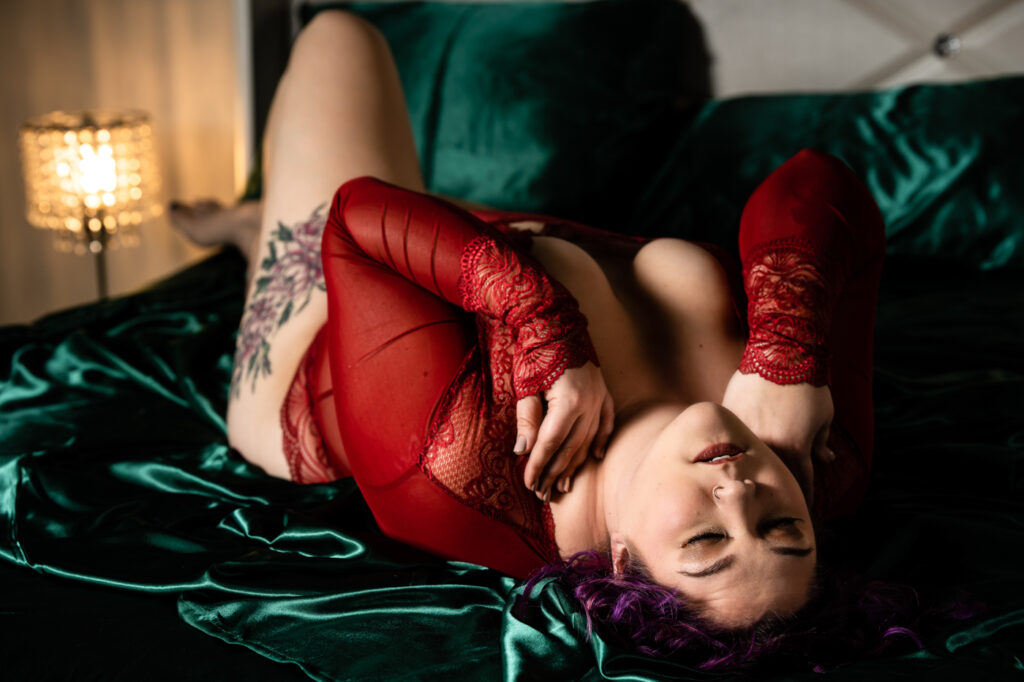 A woman in red lingerie laying on a bed with emerald green sheets. The image was taken by Inferno Boudoir in Oshkosh, Wisconsin.