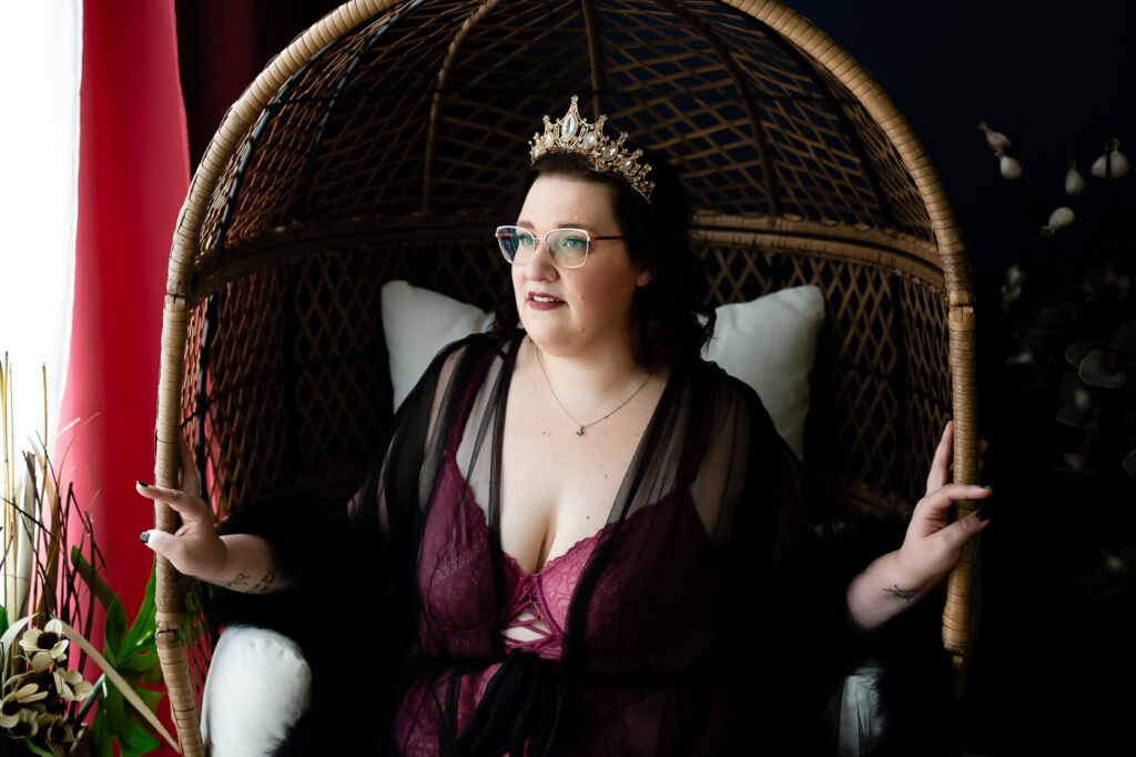 Elegant woman in black feathered robe and gold crown, sitting in an egg chair.